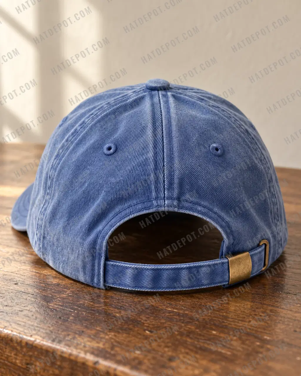 Rear detail of the denim Pigment-Dyed Washed Dad Hat on a café table, showing the faded cotton twill, sewn eyelets and self-fabric strap through an antique brass slide buckle.